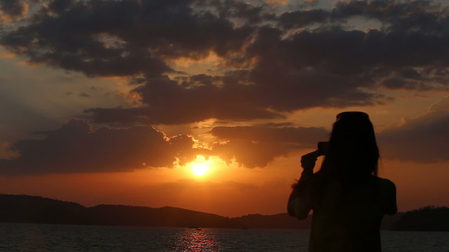 silhouette of photoing girl appears at flat horizon under fantastic sunset above sea
