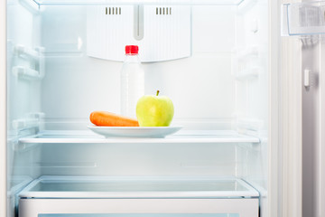 Green apple and carrot with bottle of water in refrigerator