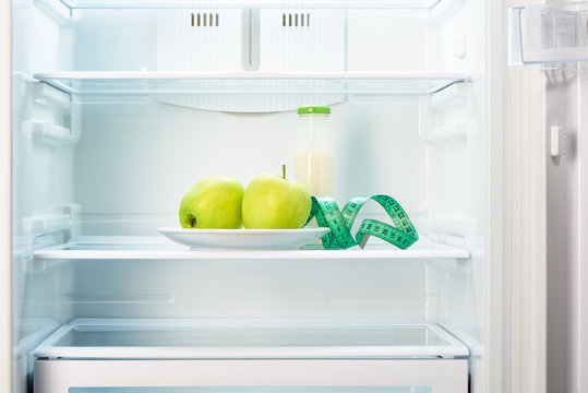 Two apples with measuring tape and glass bottle in refrigerator