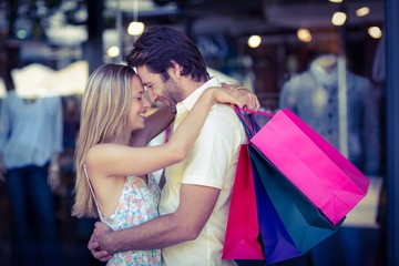 Smiling couple with shopping bags hugging closely