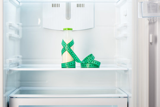 Bottle of yoghurt with measuring tape on shelf of refrigerator