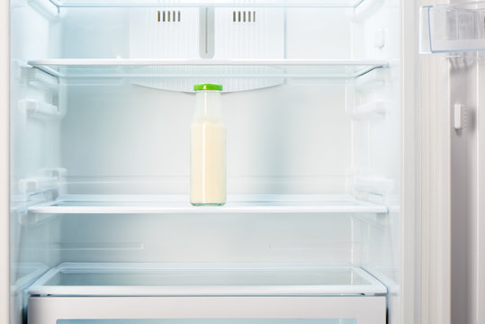 Glass bottle of yoghurt on shelf of open empty refrigerator