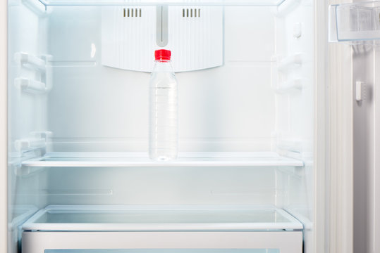 Bottle of water on shelf of open empty refrigerator