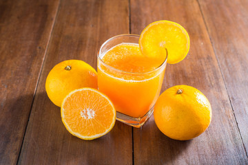 Orange juice in glass, fresh fruits on wooden background