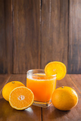Orange juice in glass, fresh fruits on wooden background