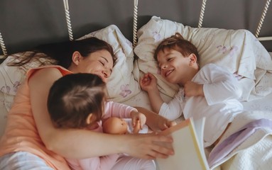 Mother reading book to her sons in the bed