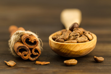 roasted coffee beans in a spoon and cinnamon sticks on wooden background, close up