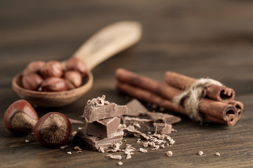 Broken chocolate bar, hazelnut and cinnamon on wooden background, close-up