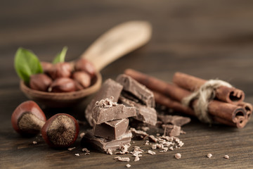 Broken chocolate bar, hazelnut and cinnamon on wooden background, close-up