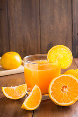 Glass of orange juice with slices on wooden background