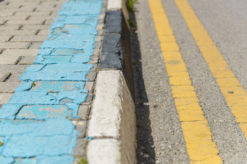 Sidewalk curb and street with different colored painted lines.