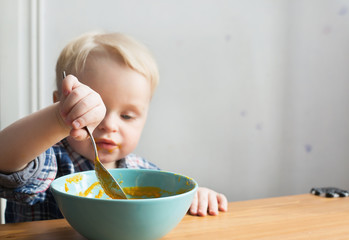 A hand of a cute little boy having soup for lunch, boy on a background unfocused