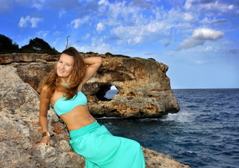 attractive woman on glamour dress leaning on rock cliff at Spain coast