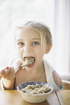 Young girl sitting at a table, eating breakfast from a bowl.