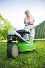 Woman in backyard garden mowing the lawn with a lawnmower - selective focus