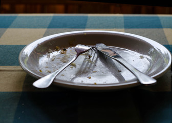 Dirty plate with crumbs,  used fork and knife, close-up, on chec