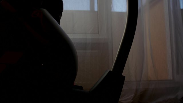 Woman exercising at home with a stationary bicycle. Dolly camera, backlit silhouette.