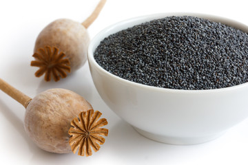 Ceramic bowl of poppy seeds with two dried pods in perspective.