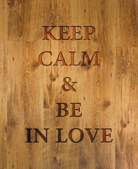 Text "Keep Calm & Be in Love" engraved in wooden background