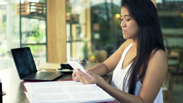 Young female student doing homework with smartphone in cafe 
