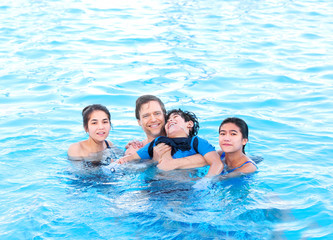 Multiracial family swimming together in pool. Disabled youngest