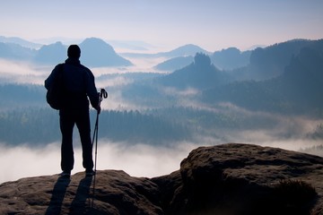 Dark silhouette of hiker with poles in hand. Sunny spring daybreak in rocky mountains. Hiker with...