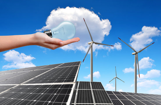 Hand holding lightbulb in the background solar  panels and wind turbines
