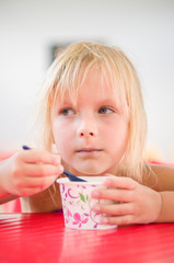 Adorable girl eat chocolate ice cream in cup with spoon in cafe