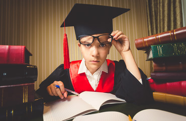 genius girl in graduation cap looking through eyeglasses at came