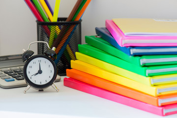 Black alarm clock and multi colored books in stack
