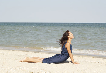 Fototapeta na wymiar Young beautiful woman doing yoga at seaside in blue dress