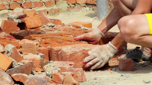 hands are bricks in construction/On the construction of a hand to a red brick from the pile and carry