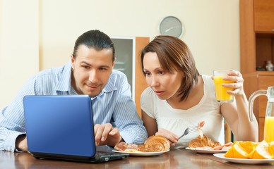 Obraz na płótnie Canvas Happy ordinary couple using laptop during breakfast