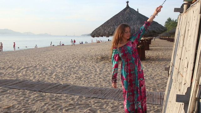 girl in long dress and red hat poses by beach bamboo tower