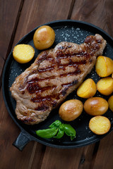 Above view of grilled striploin steak with potatoes and basil
