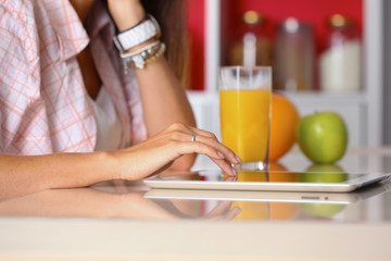 Woman using a tablet computer while drinking tea in her kitchen