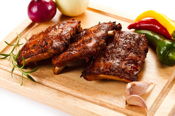 Barbecued ribs with vegetables on cutting board 