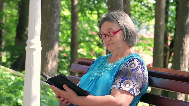 Senior woman reading bible on the bench in the park.