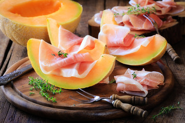 Italian prosciutto with melon with fresh thyme on rustic wooden kitchen table - obrazy, fototapety, plakaty