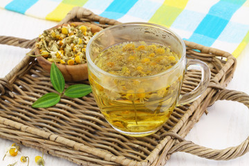 Chamomile tea in transparent glass on wicker tray
