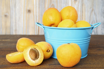 Fresh sweet apricots in a blue metal bowl on wooden background                             