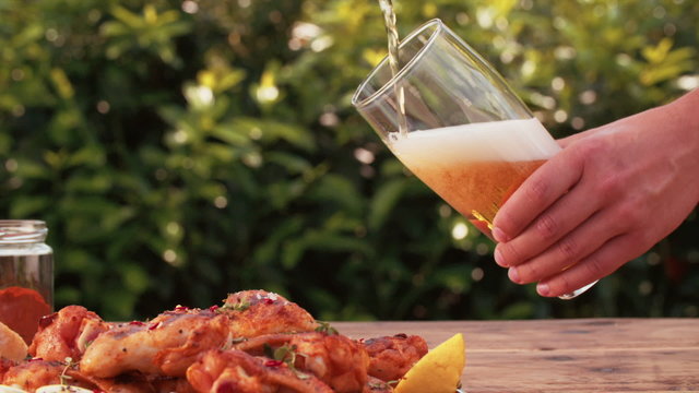 Man pouring glass of beer with chicken wings in foreground