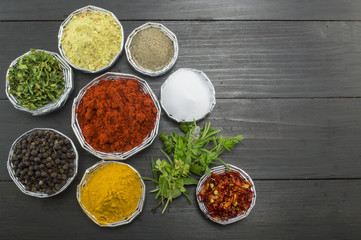 Different spices in shiny bowls on a dark wooden table
