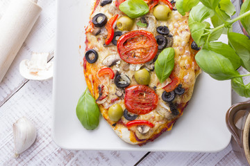 pizza with tomatoes, mushrooms, olives and peppers served on a plate on a wooden table