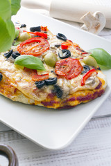 pizza with tomatoes, mushrooms, olives and peppers served on a plate on a wooden table