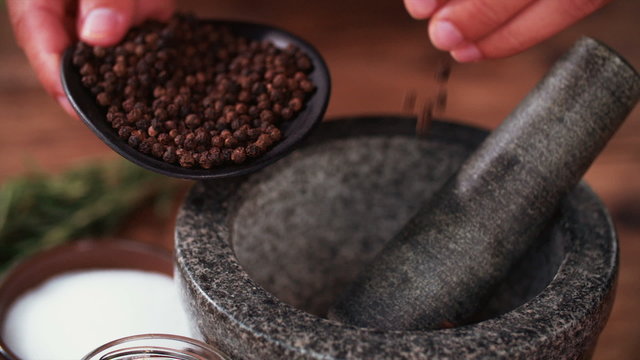 Black peppercorns being put into a mortar and pestle
