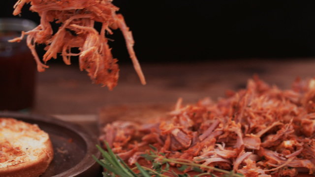 Tender pulled pork being put on a toasted burger bun