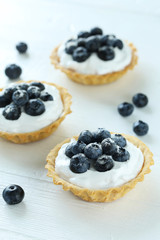 Dessert tartlets with blueberries on white wooden background