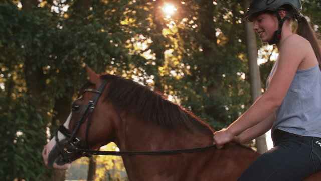 Girl riding her horse down a sunlit park lane