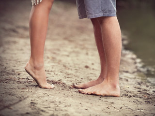 Fototapeta na wymiar Close-up of barefoot pair of human's feet on sandy beach standing next to the lake